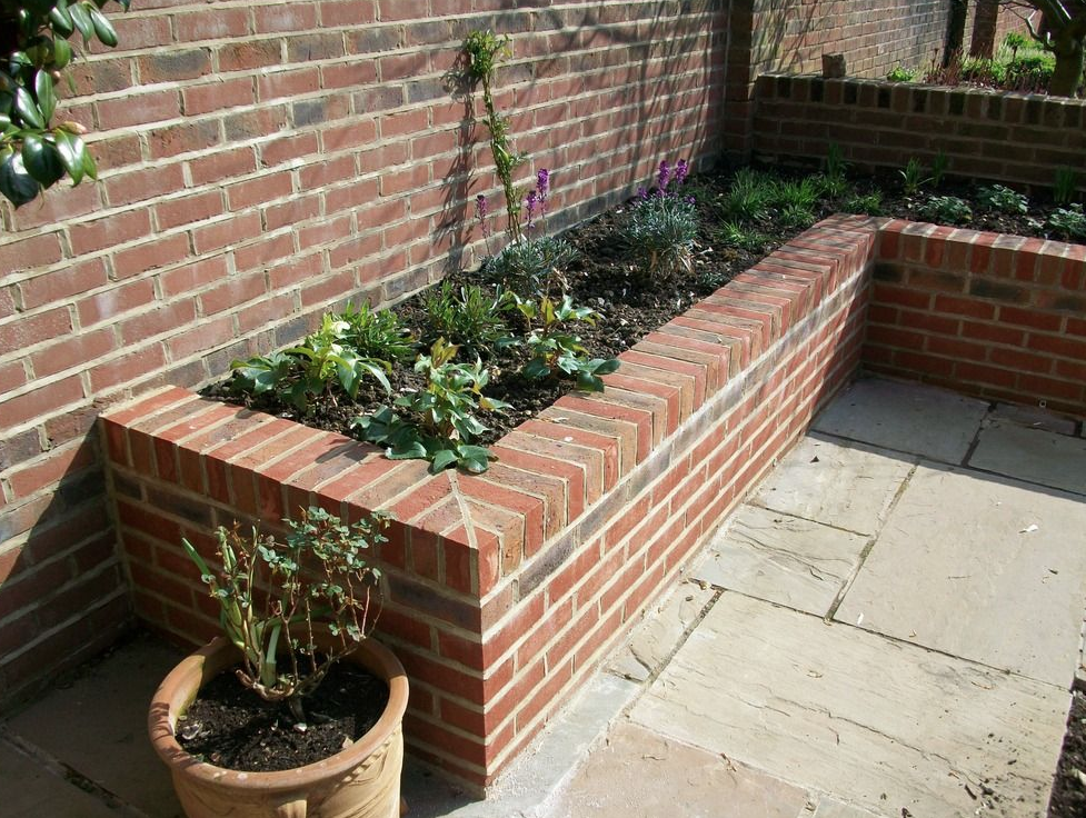 Corner raised brick planter bed built against a garden wall