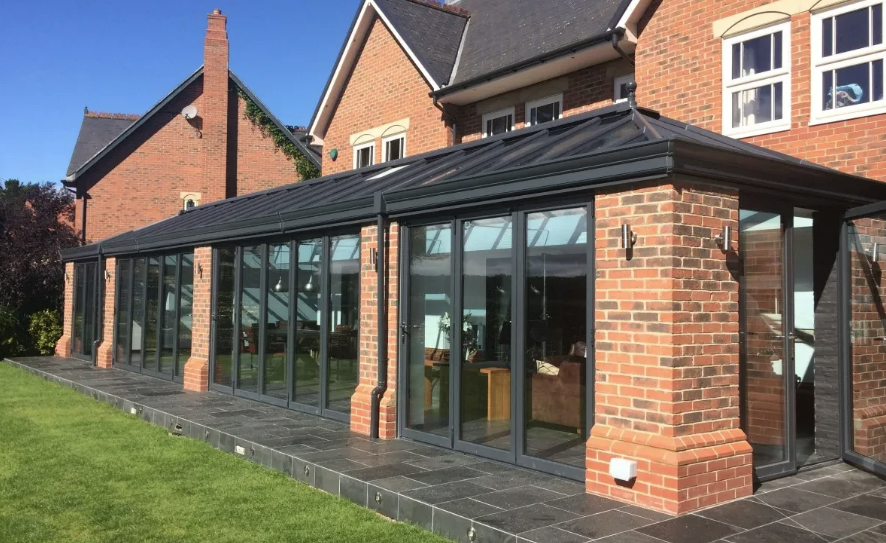 Full-width orangery with dark frames on brick piers and plinth