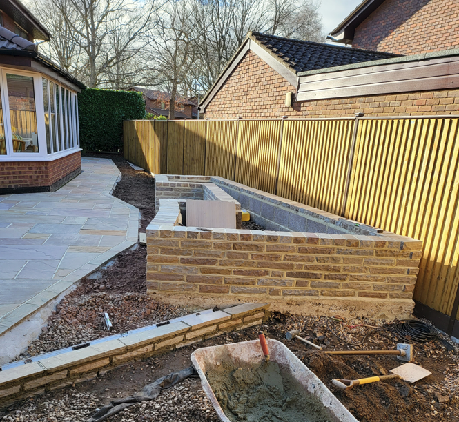 Stone-faced raised beds under construction beside a new patio
