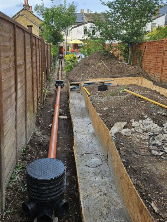 Garden trench laid with orange underground drainage pipe and chamber