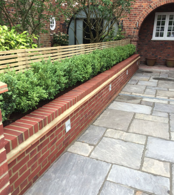 Long curved raised bed in red brick with timber slat screen